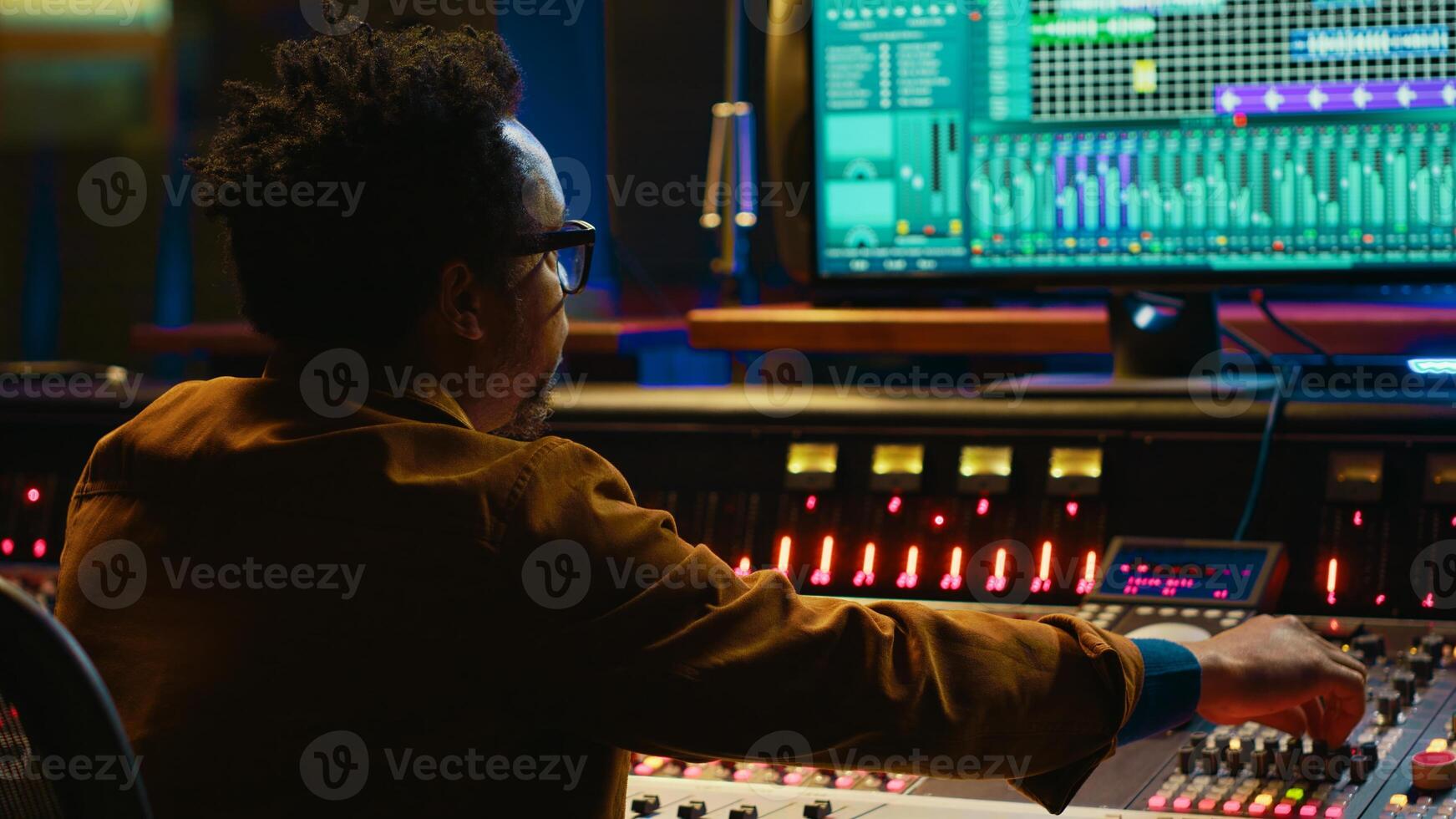 African american producer working at mixing panel in recording studio. Using control desk and digital audio workstation software on pc to edit and process tracks, post production concept. Camera A. photo
