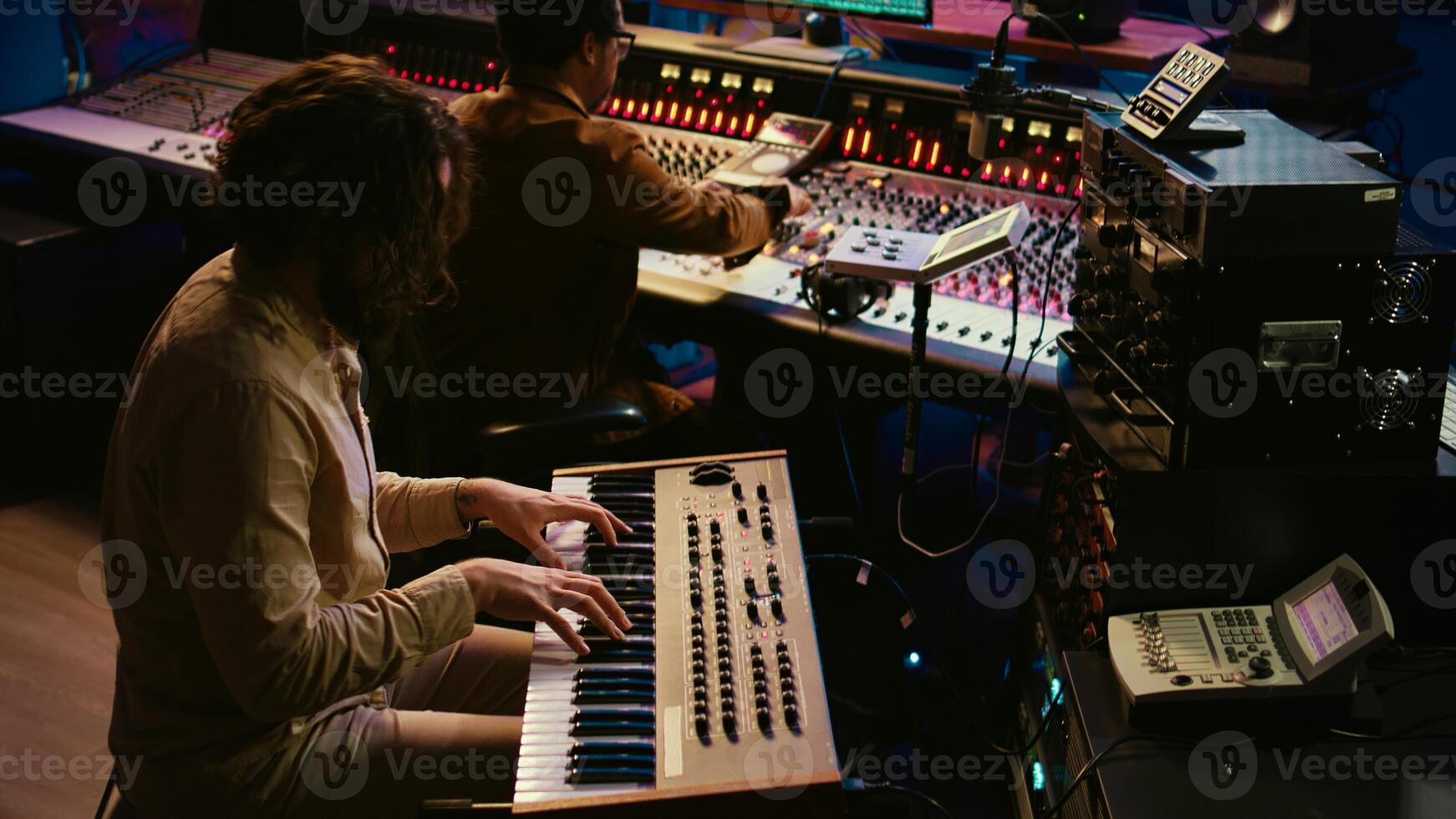 Skilled artist singer recording songs on electronic midi controller, singing on piano and creating tracks with audio engineer. Young musician composer editing music on console. Camera B. photo