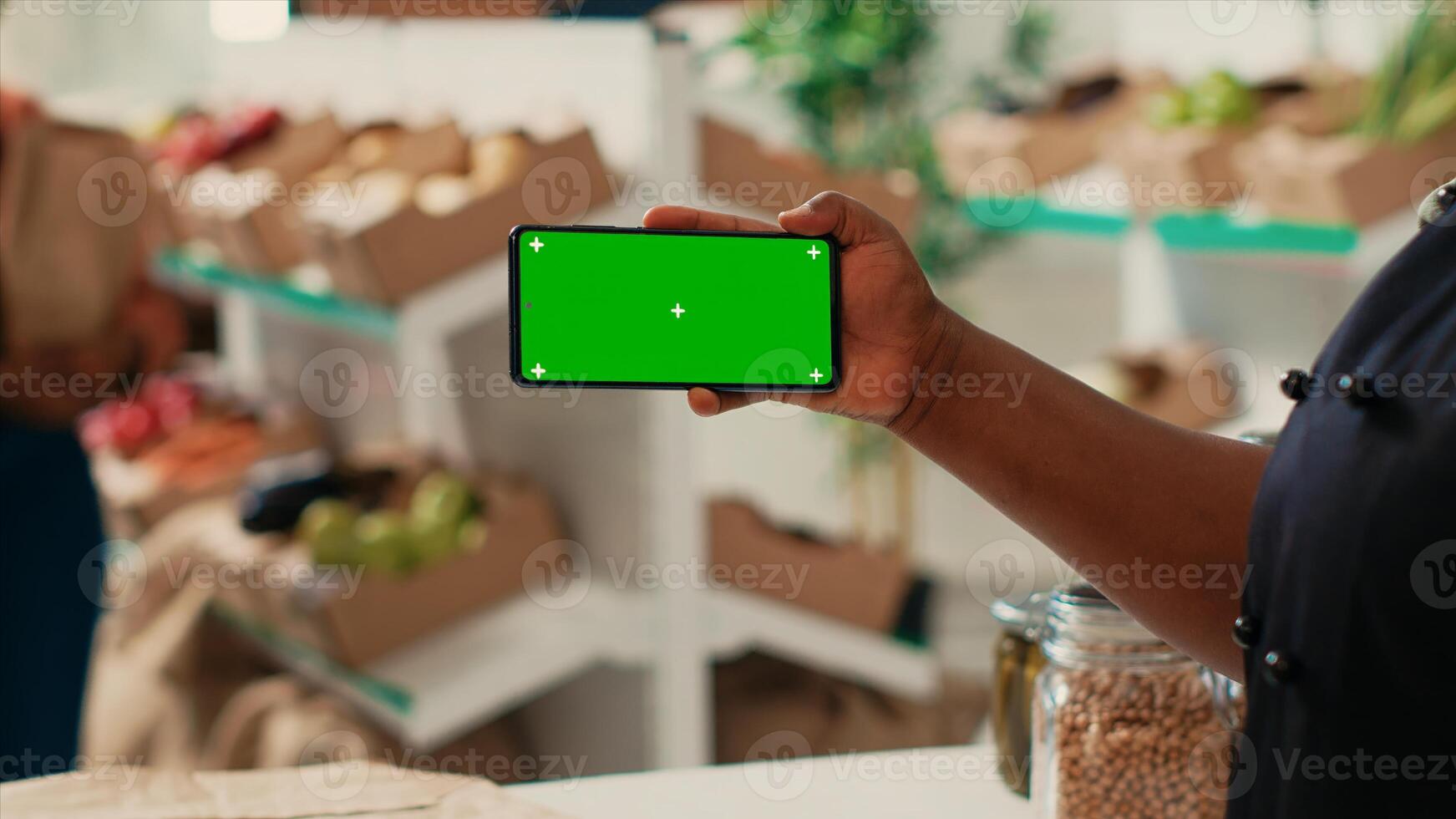 African american owner using greenscreen display at checkout, holding isolated mockup template while trying to sell organic produce at local shop. Merchant showing chromakey layout. photo