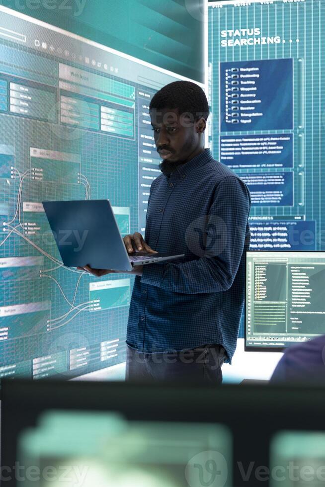 Governmental hacking specialist targeting sensitive information through high tech cyber attacks, digital espionage with a laptop and big screen. Hacker working on national security and data privacy. photo