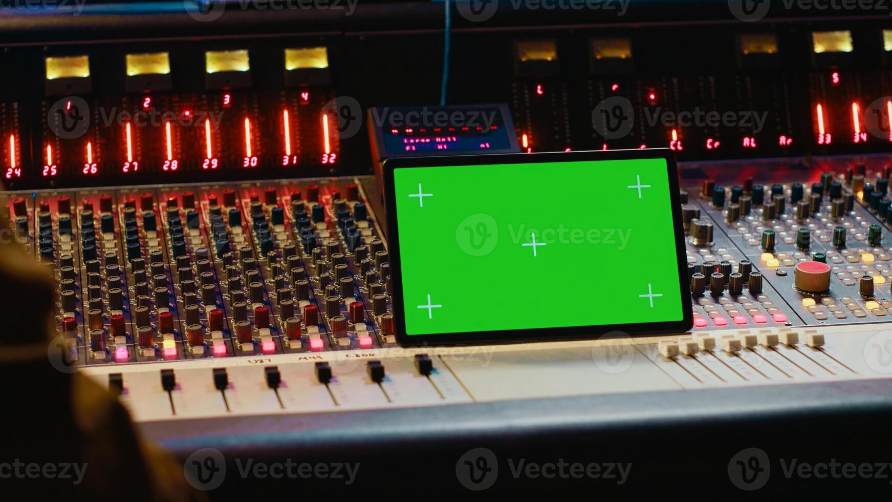 Music producer holding a tablet with greenscreen display on mixing console in control room, twisting knobs and pushing faders to edit audio recordings. Processing sounds. Camera A. photo