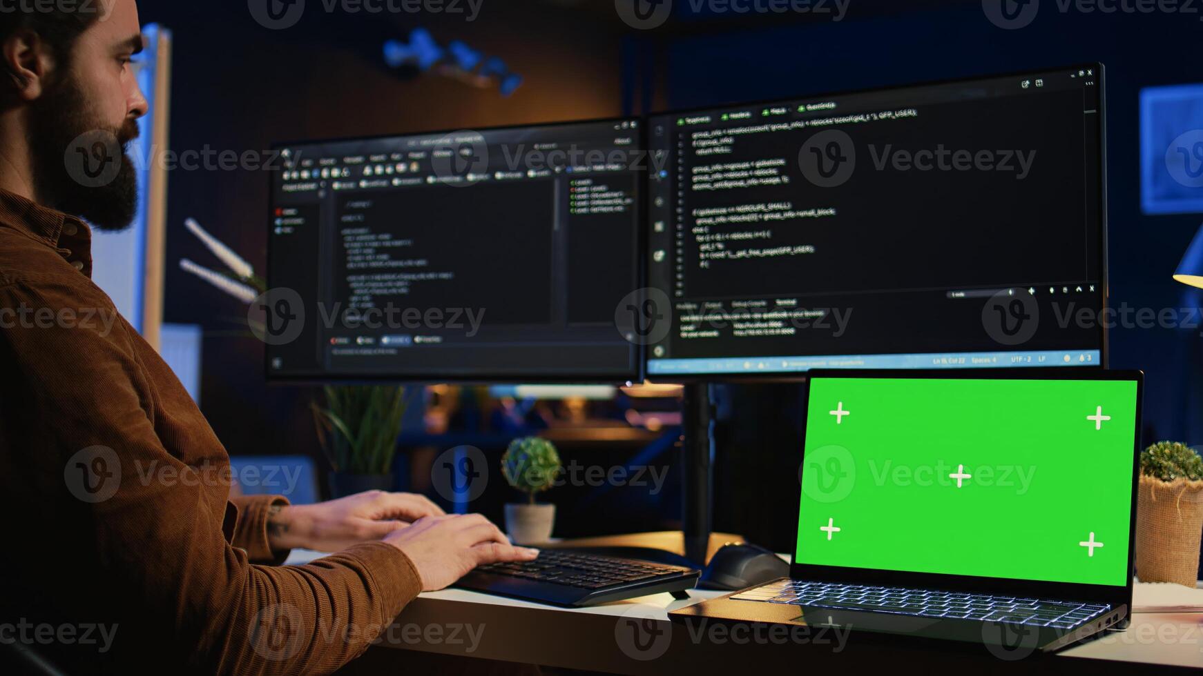 Programmer coding on computer next to isolated screen laptop in home office, developing software application. Teleworking IT specialist doing programming on PC near chroma key notebook, camera B photo