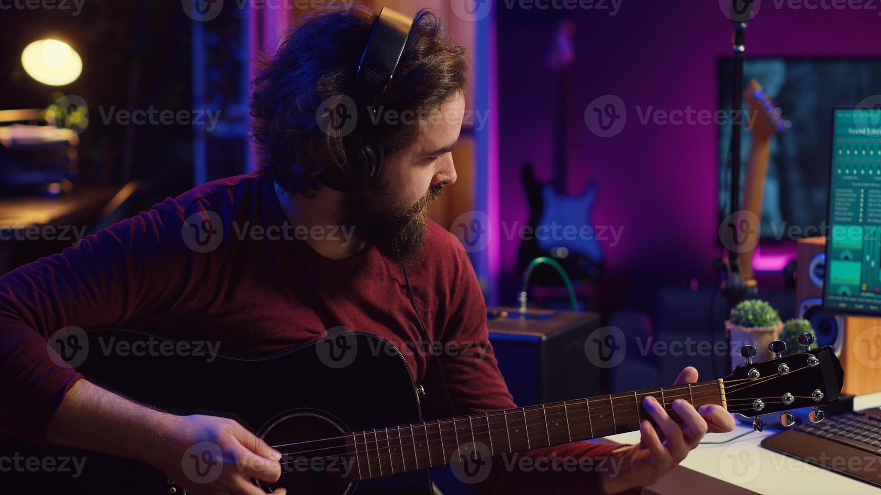 Sound engineer playing acoustic guitar and using mixing console to record music, adjusting volume and adding sound effects to tunes. Artist works with digital audio workstation software. Camera A. photo