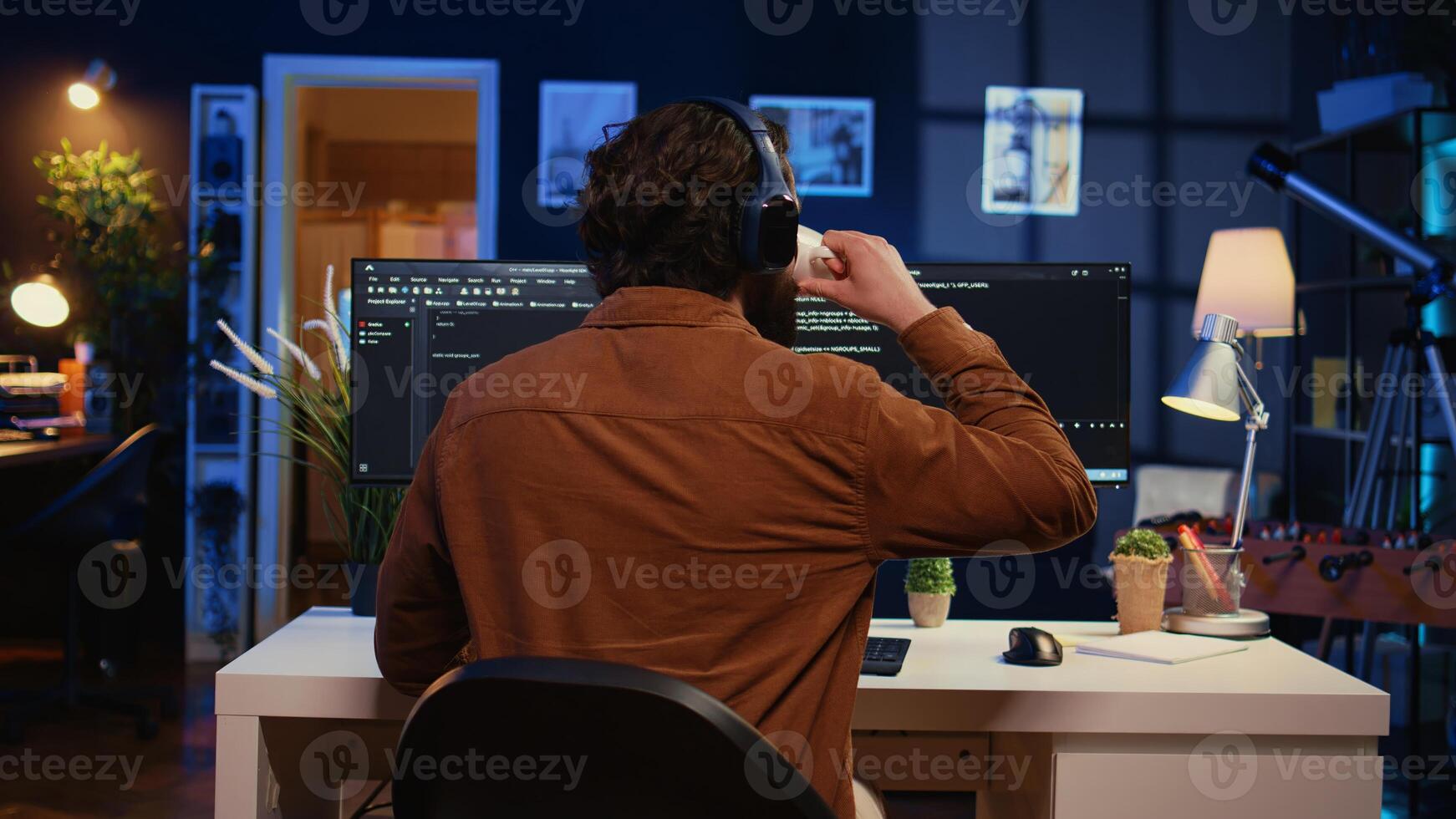 Man doing IT support job from apartment office, drinking cup of coffee and listening music while coding. Developer with headphones on enjoying hot tea and writing code on computer, camera B close up photo