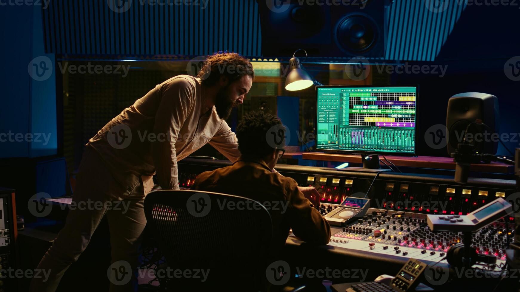 Tracking engineer collaborating with musician to edit sounds in studio control room, recording tunes to create a new album. Audio expert operating audio mixer and controller. Camera B. photo