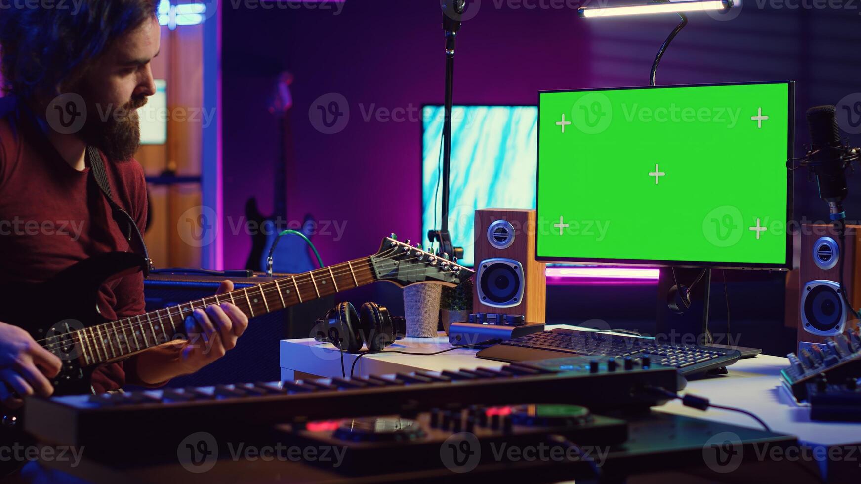 Male singer learning to play a new song on acoustic guitar, using greenscreen on computer to watch online tutorials. Artist songwriter practicing with his instrument in home studio. Camera A. photo