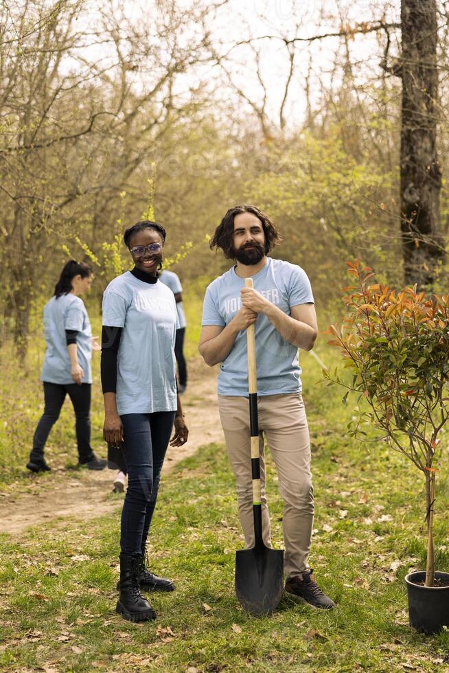 Portrait of diverse activists participating at conservation project, digging holes with a shovel and planting trees to restore nature. Reforestation and litter cleanup, protecting wildlife. photo