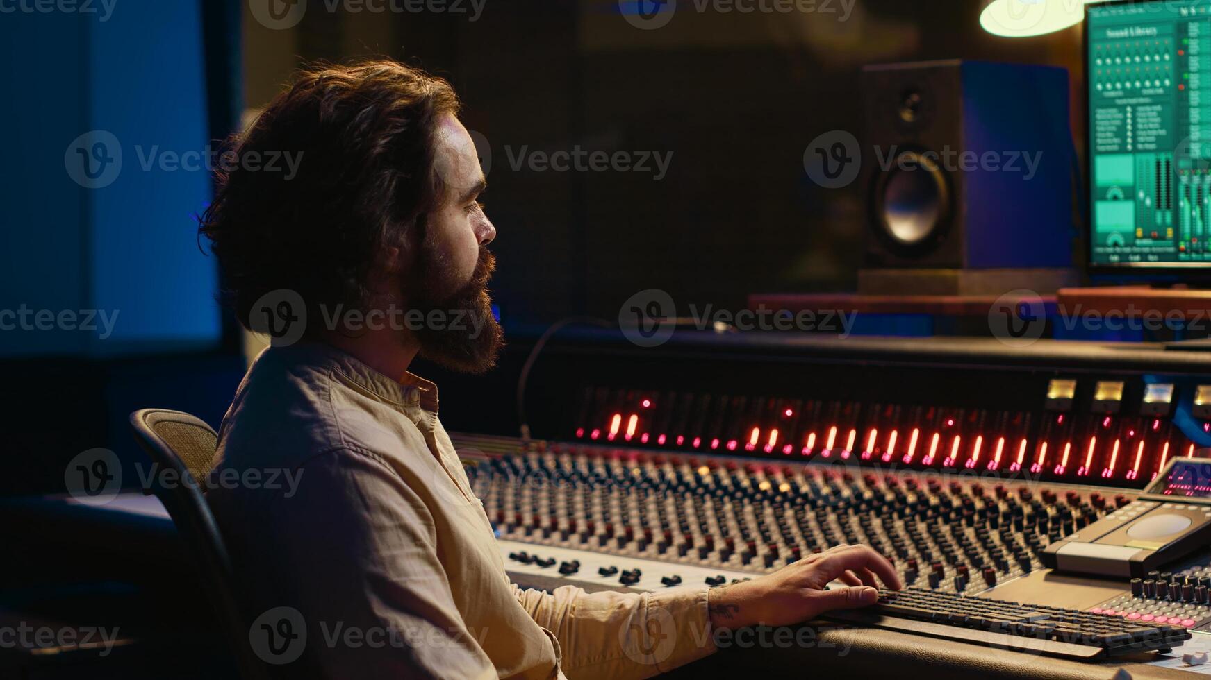 Sound designer processing and mixing tunes in control room, working on a new album in professional recording studio. Audio expert using control panel board with buttons and sliders. Camera A. photo