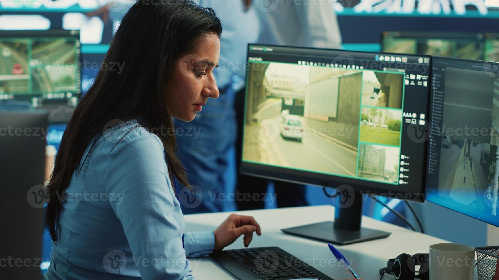Indian woman operator locating delivery truck and offers gps coordinates of the shipment location. Control center employee consults satellite map and CCTV system for routes. Camera A. photo