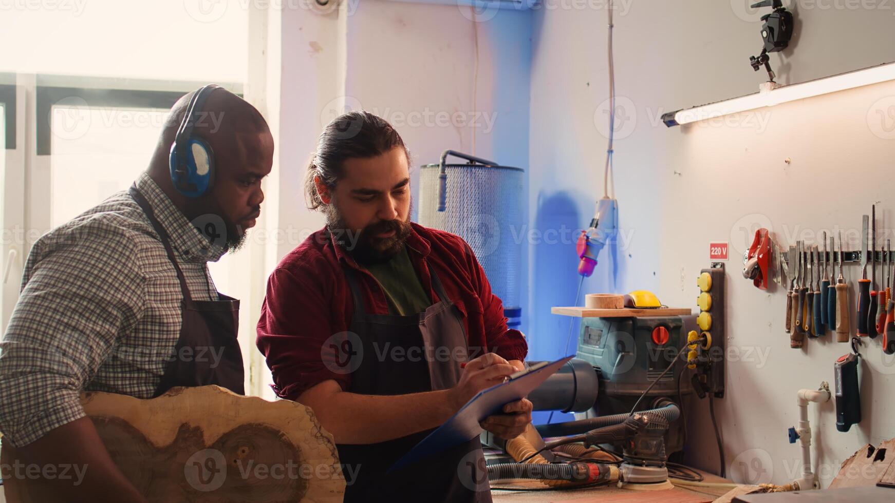 Craftsperson and colleague look over technical schematics to make commissioned wooden object. Manufacturer and coworker analyze blueprints to execute furniture assembling woodworking project, camera B photo