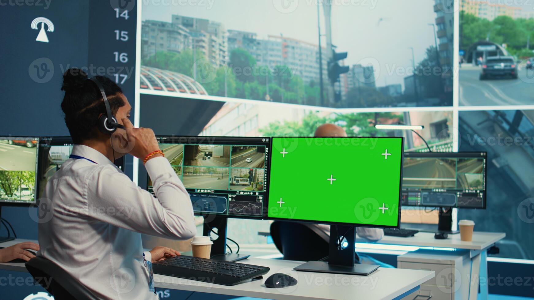 Indian operator monitors traffic next to a greenscreen on display, following surveillance footage from satellite radar cameras. Agency employee works with city CCTV system. Camera B. photo