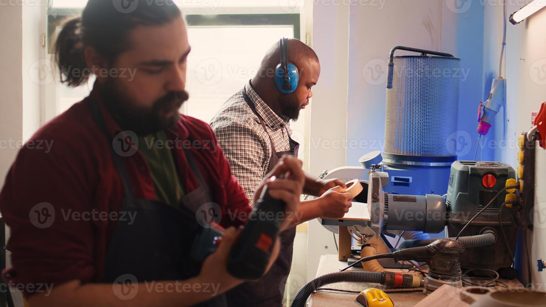 Carpenter changing power drill head into suitable one for task ahead, making holes into timber block. Cabinetmaker in assembly shop preparing electric gear tool to use for commissioned job, camera B photo