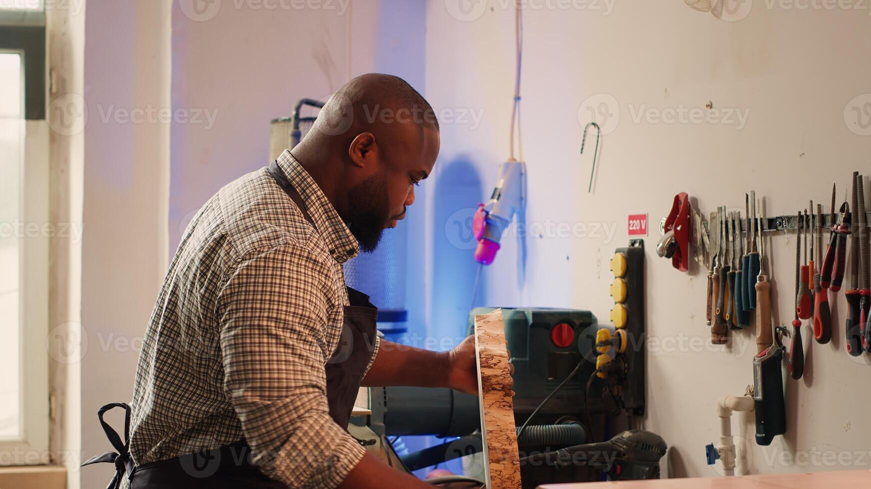 Carpenter in woodworking shop spinning wood block around, inspecting it before assembling furniture. BIPOC cabinetmaker in joinery studio evaluating lumber block, checking for damages, camera A photo