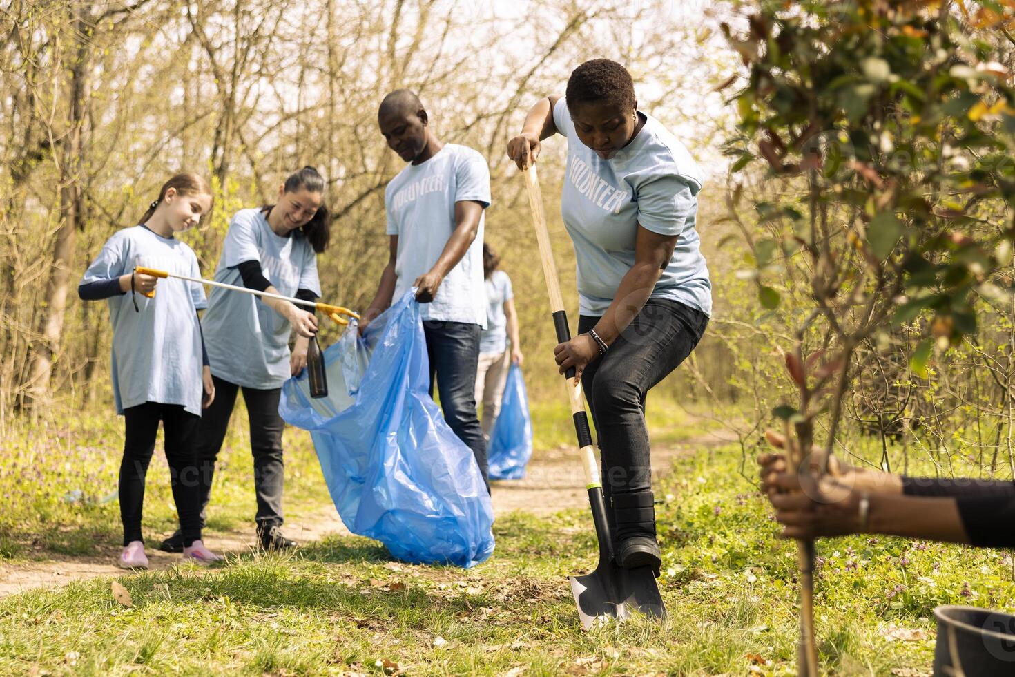 Diverse people cleaning up garbage in a disposal trash bag, environmental preservation mission. Activists clearing the forest natural habitat, collecting rubbish with long claw tool. photo