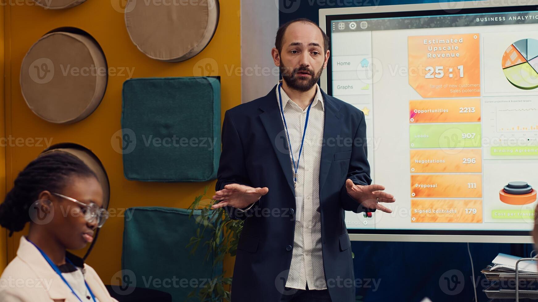 Management consultant gathering his employees for a status update meeting in boardroom, interactive presentation with the latest data. Success metrics and key performance indicators. Camera A. photo