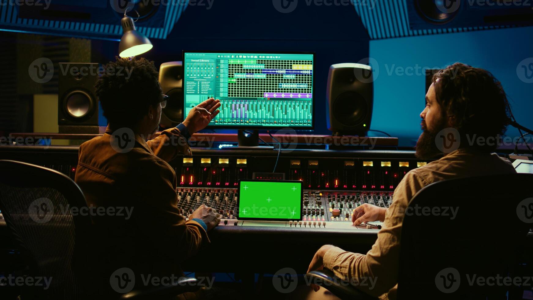 Professional engineer and musician mixing tracks next to isolated display on tablet, editing audio after recording session to produce a hit song. Artist collaborates with sound designer. Camera B. photo