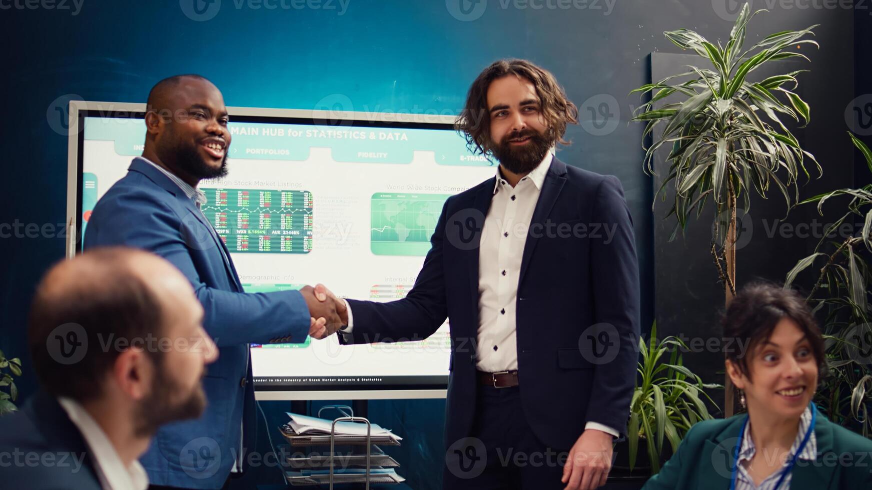 Business partners celebrate the beginning of a new project between their companies, shaking hands in a meeting. Leaders forging an agreement to develop the corporation and collect resources. Camera B. photo