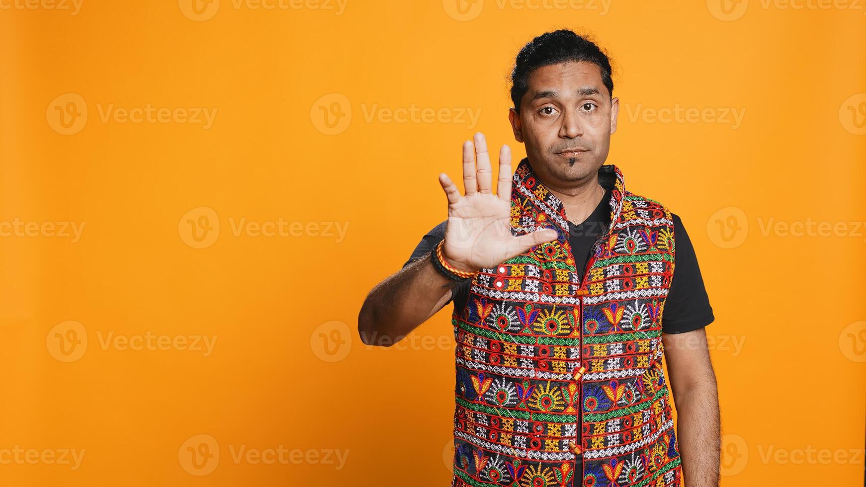 Stern indian man doing stop hand gesture sign, complaining. Authoritative person doing firm halt sign gesturing, wishing to end concept, isolated over studio background, camera B photo