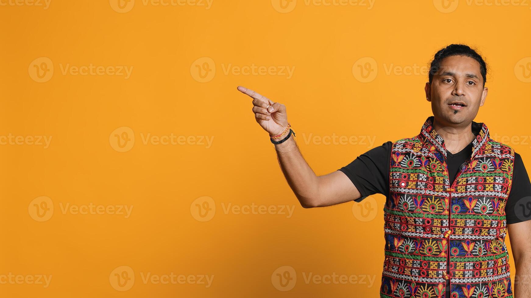 Salesman pointing around with finger, doing recommendation, talking with audience. Indian person showing copy text, doing advertisement, isolated over studio background, camera A photo