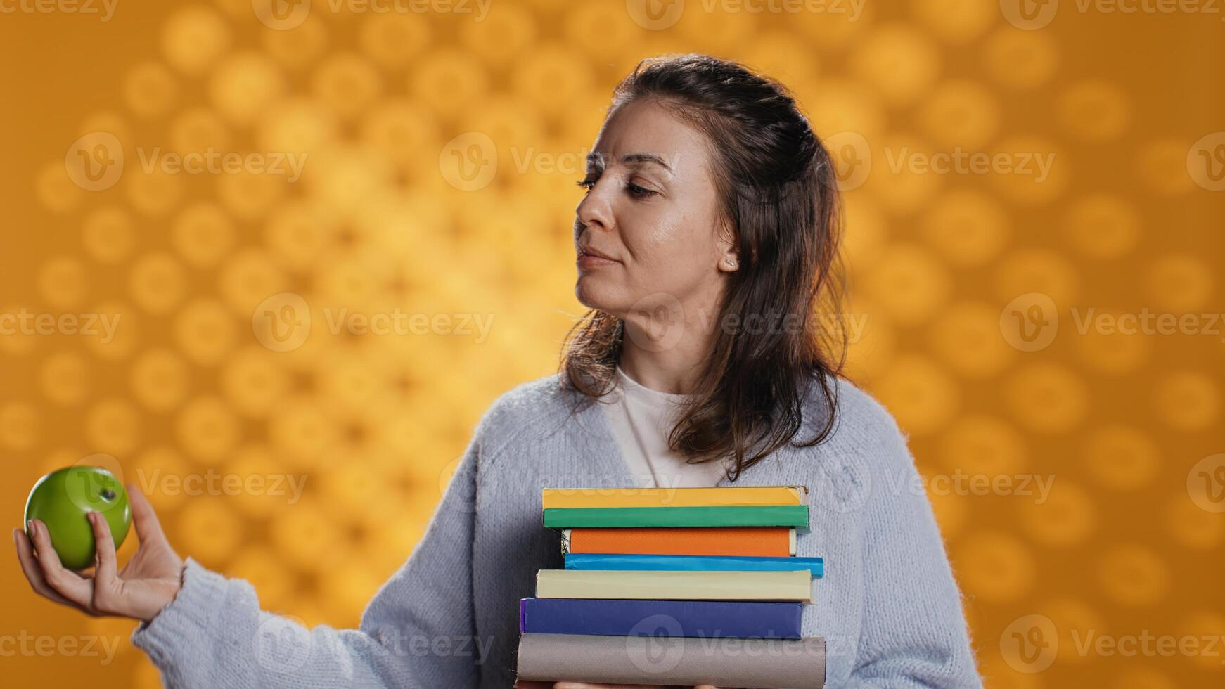 Happy woman holding books and playing with apple, conveying joy of reading and eating healthy, studio background. Cheerful person with novels and fresh fruit, good lifestyle concept, camera B photo