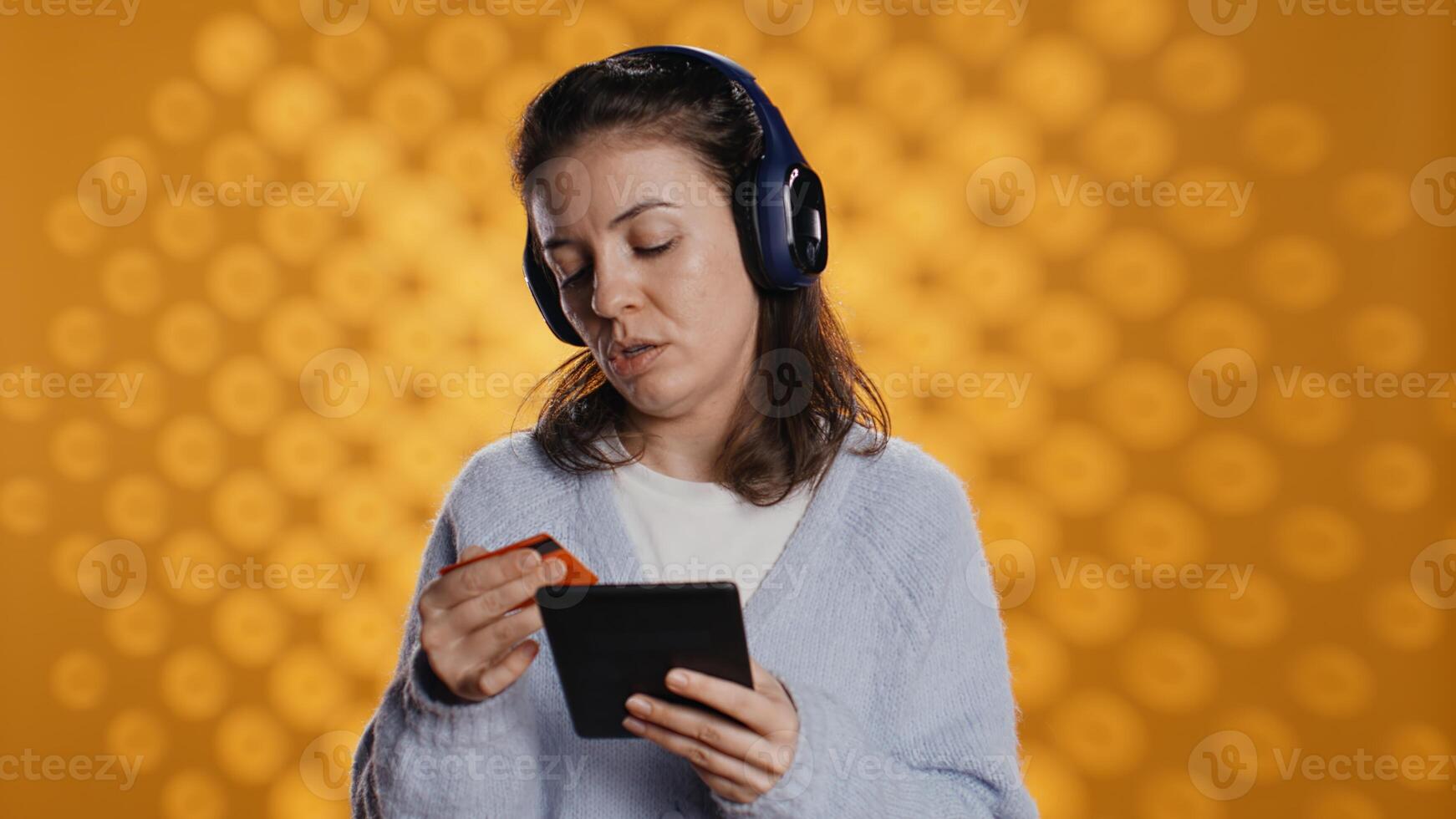 Woman reading ebook on ereader and listening music purchasing books online. Person with tablet looking to buy digital novel with credit card, hearing songs in headphones, studio background, camera B photo