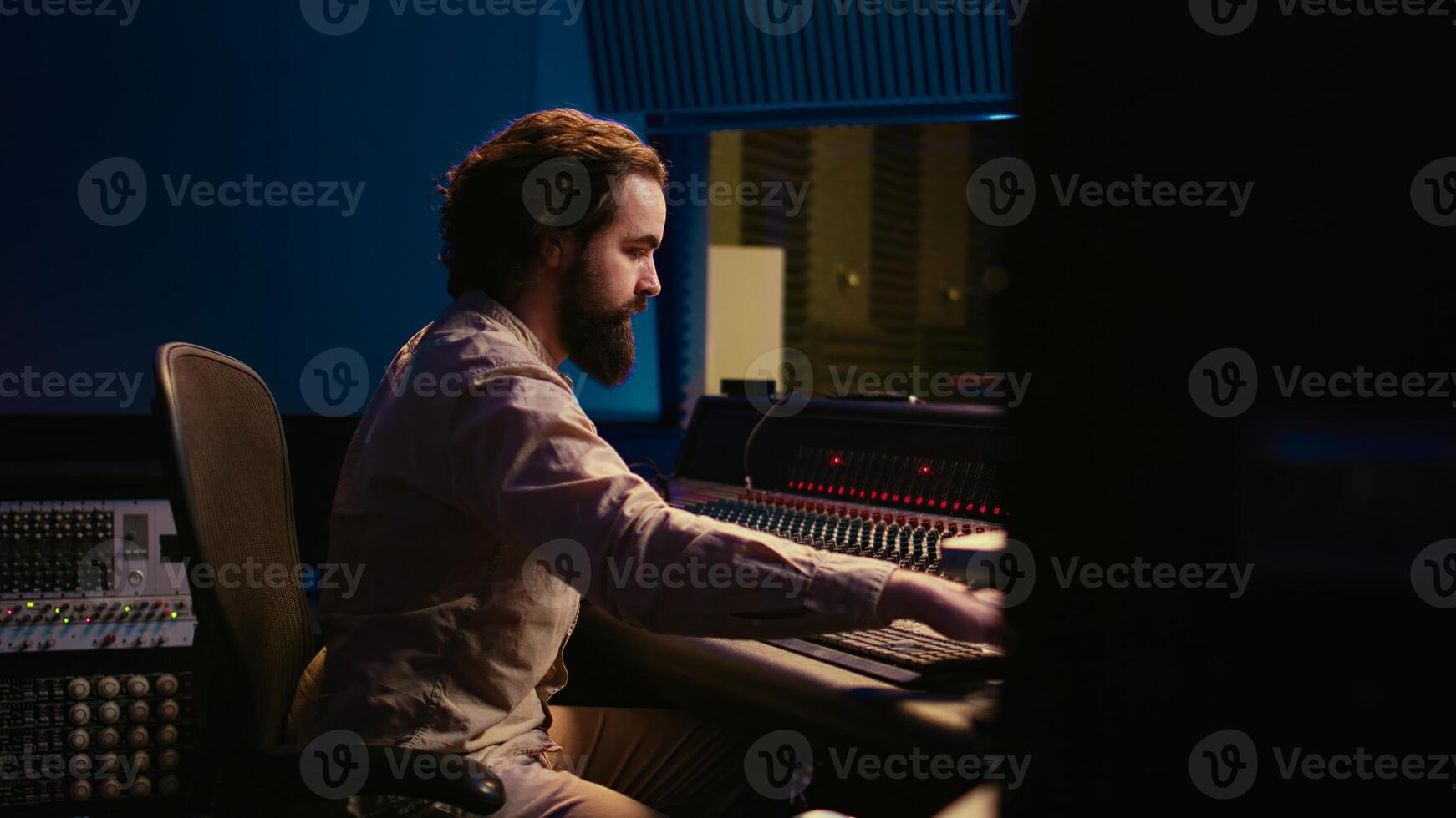 Portrait of audio technician adjusting volume levels on recordings by using pre amp knobs and fader on control room board. Music producer working on mix and master techniques. Camera B. photo