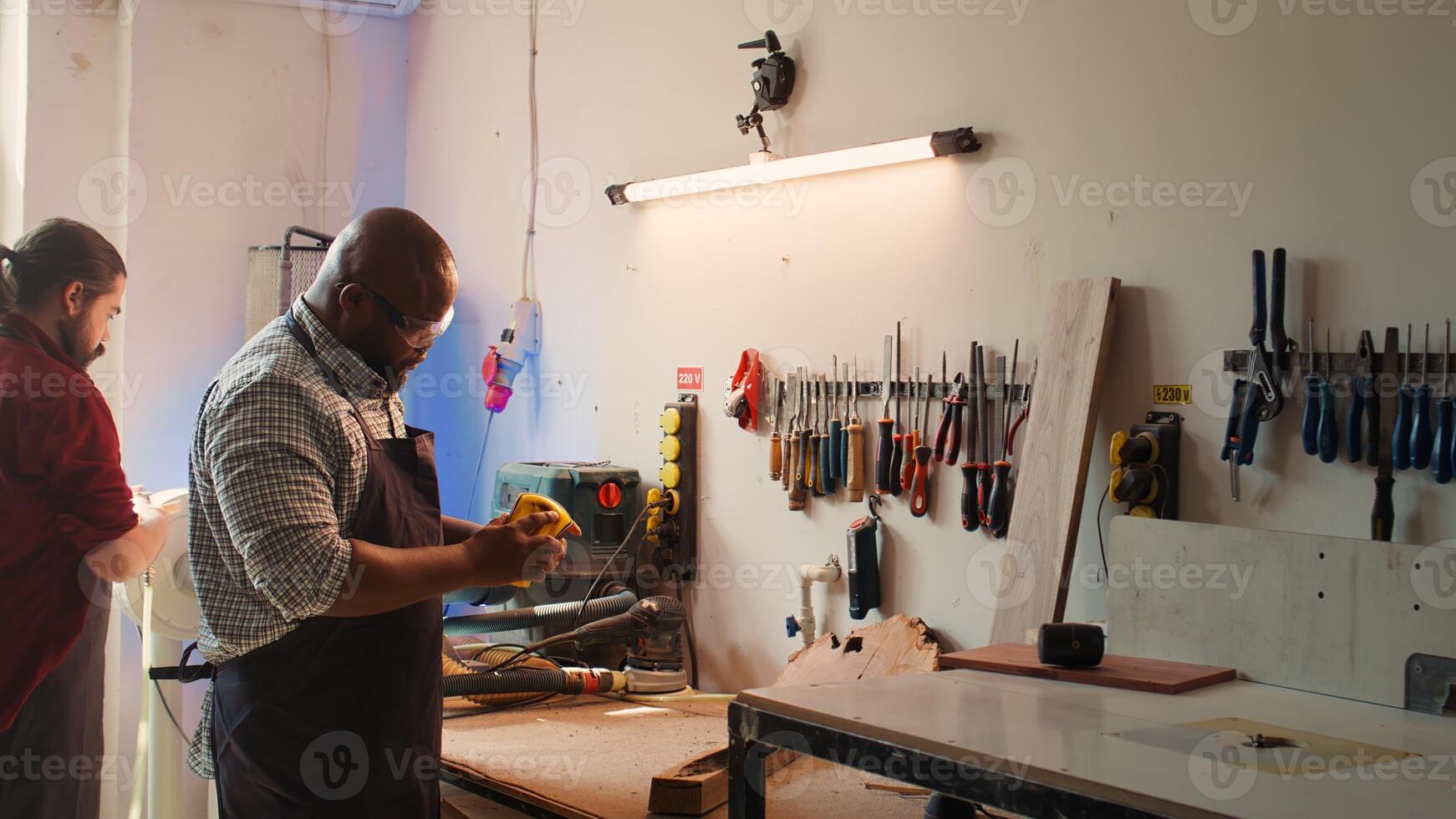 African american artisan in studio using sandpaper for smoothing wooden surface, creating wood art designs. BIPOC person using sanding sheets to refurbish damages suffered by timber block, camera B photo