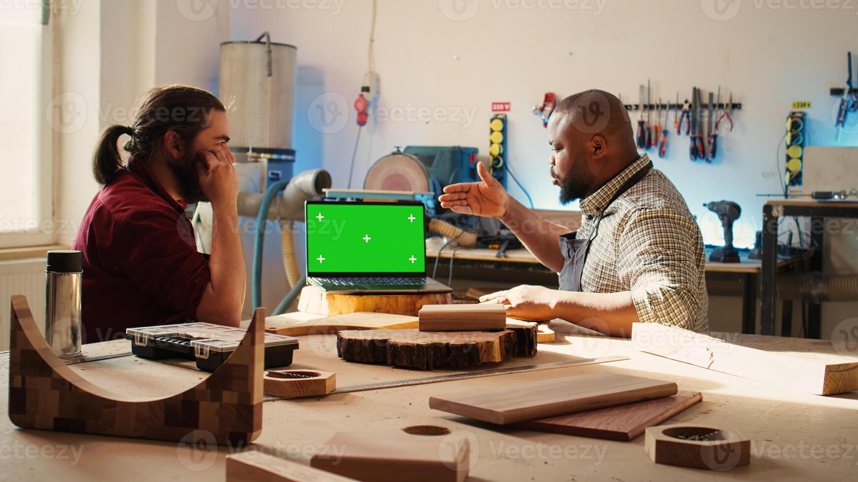 Woodworker looking over blueprints on green screen laptop in CAD software with apprentice. Craftsperson and coworker designing custom 3D furniture on chroma key notebook in studio, camera B photo