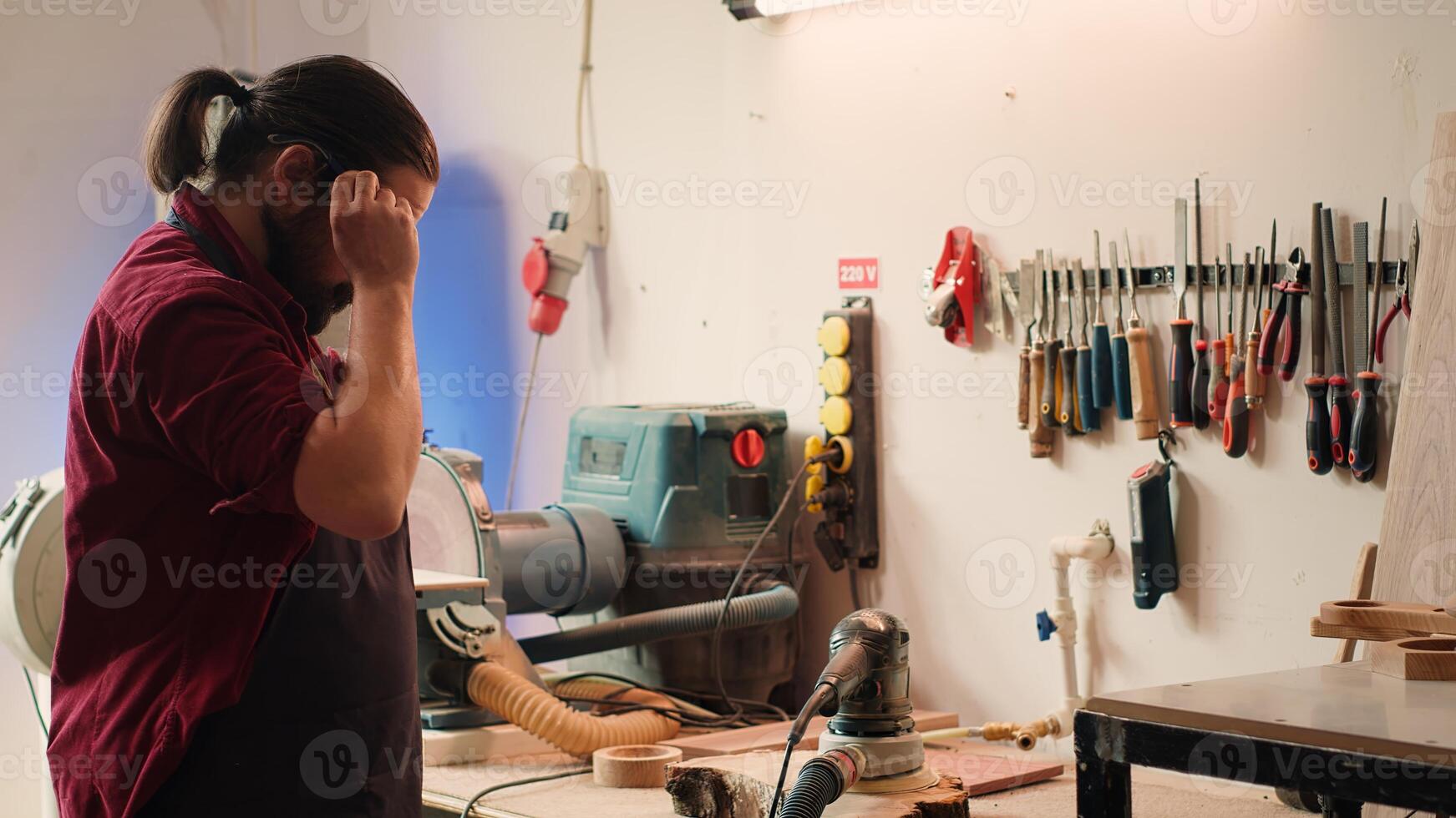 Artisan uses safety goggles to prevent workplace accidents while removing imperfections on wood. Man wearing protective equipment to avoid injury while using angle grinder to sander plank, camera A photo
