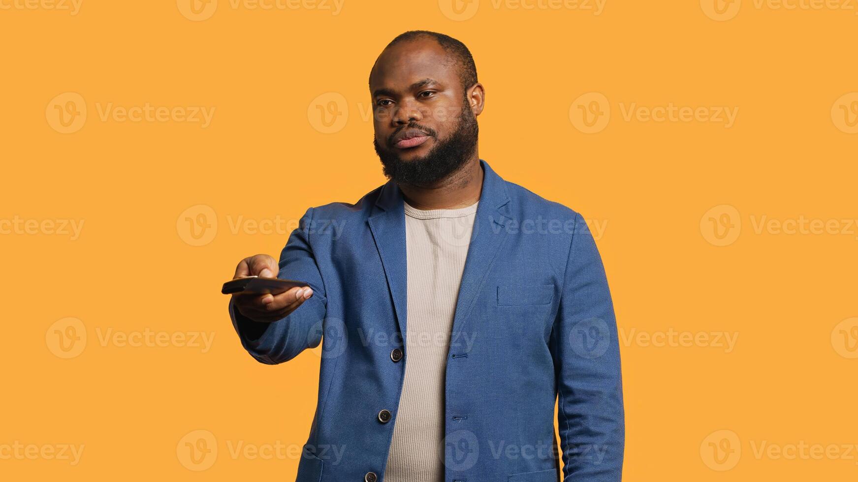 Man zapping through channels, watching news broadcast, isolated over studio background. African american person using remote control to select television station to enjoy, camera A photo