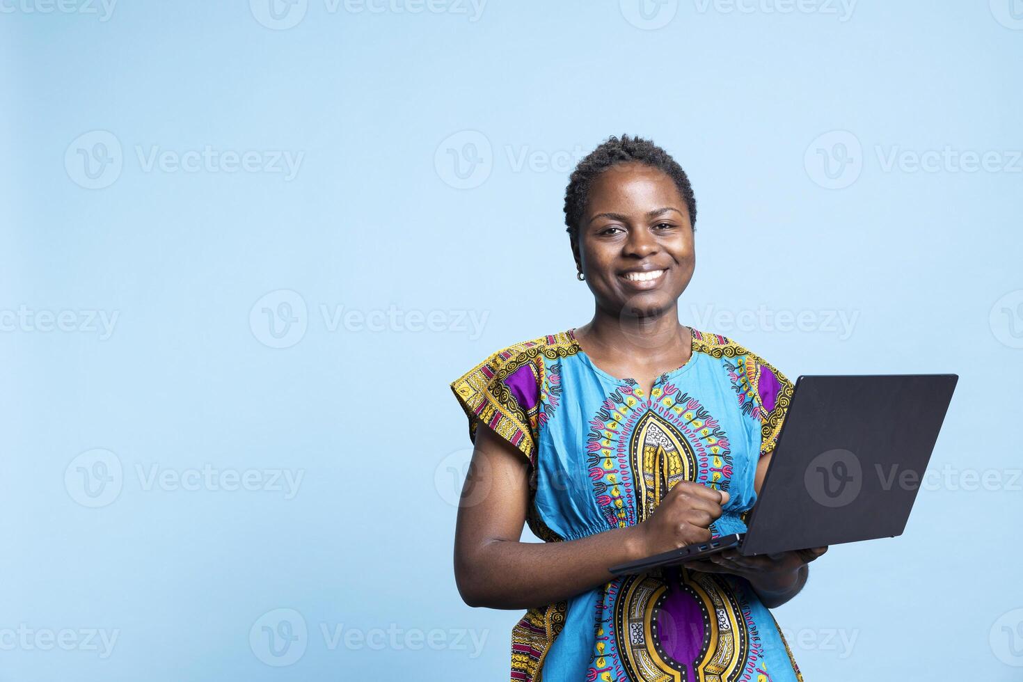 Modern web user navigating on social media network in studio, holding laptop to browse information online. African american girl uses wireless electronic device, posing in front of camera. photo