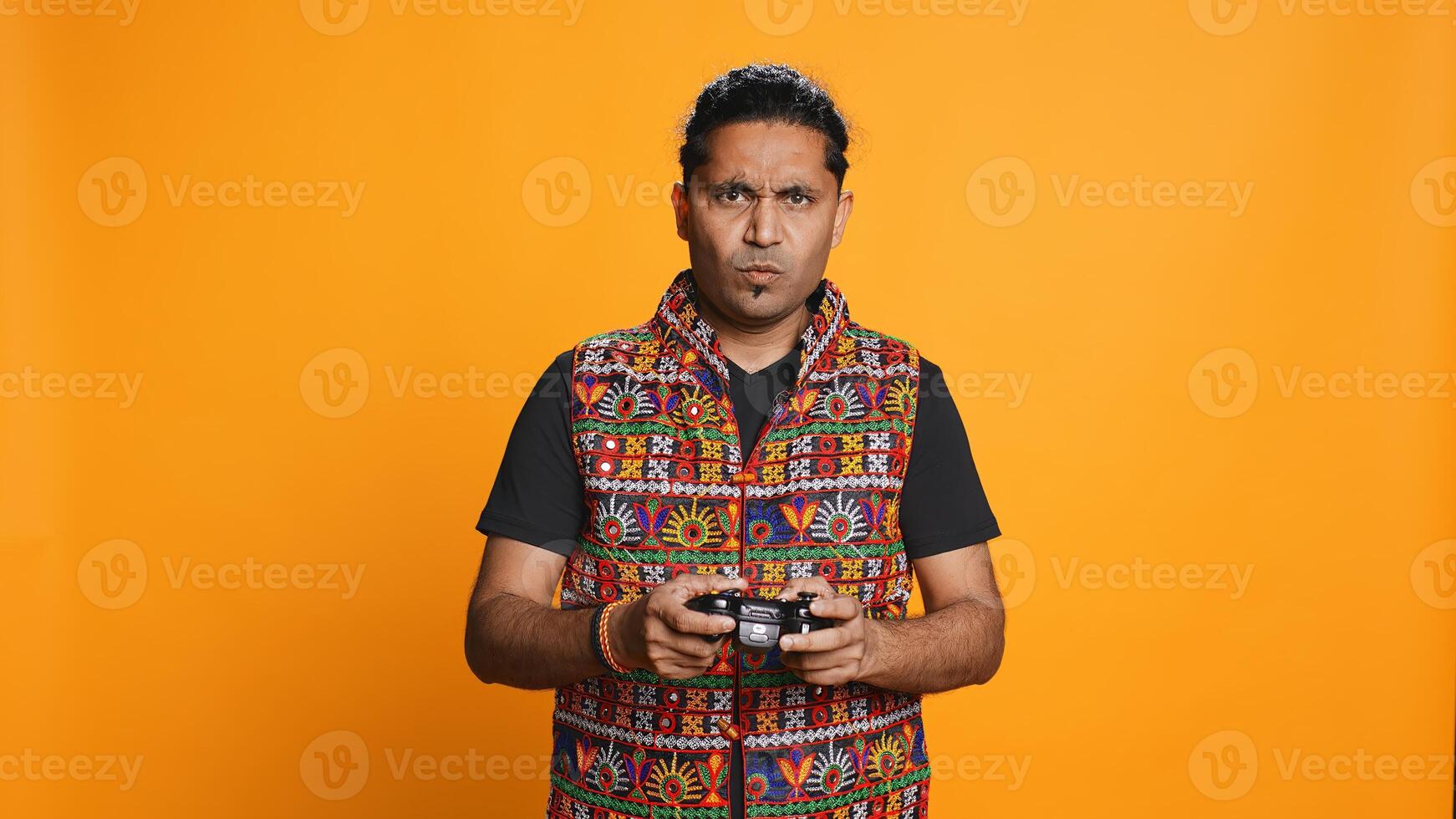 Cheerful man playing videogames with controller, studio background. Indian gamer smiling, having fun by participating in PvP online multiplayer game using console system, camera B photo