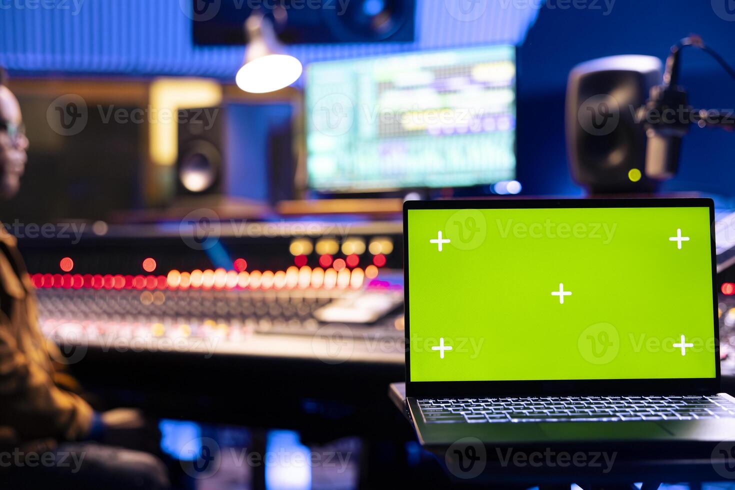 Focused audio engineer recording tracks on control panel board next to laptop with greenscreen, adjusting volume levels on mixing console. Sound designer creating music for his new album. photo