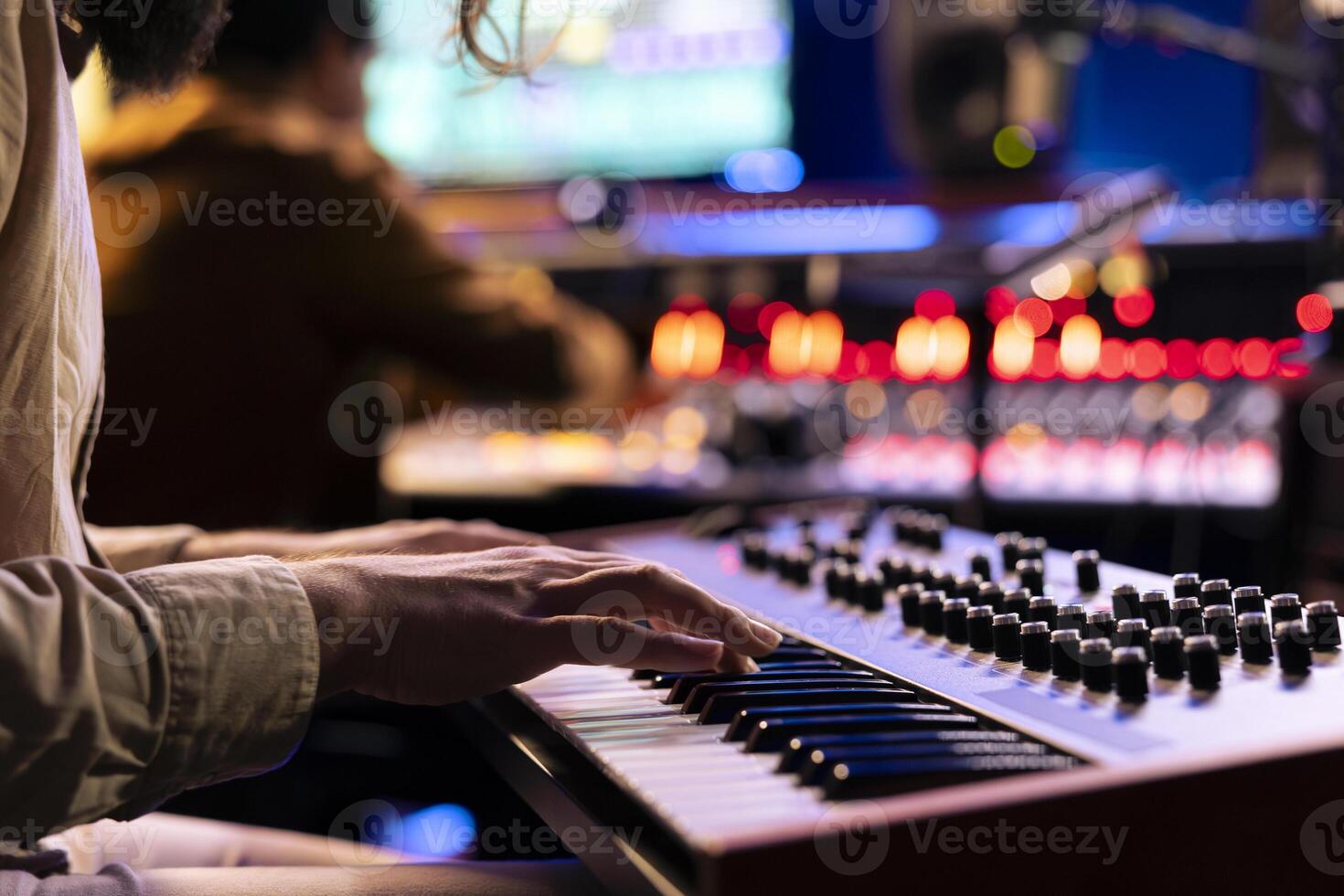 Male musician performing a hit song on electronic keyboard in recording studio, playing notes on midi controller to edit in post production. Artist singing in control room. Close up. photo