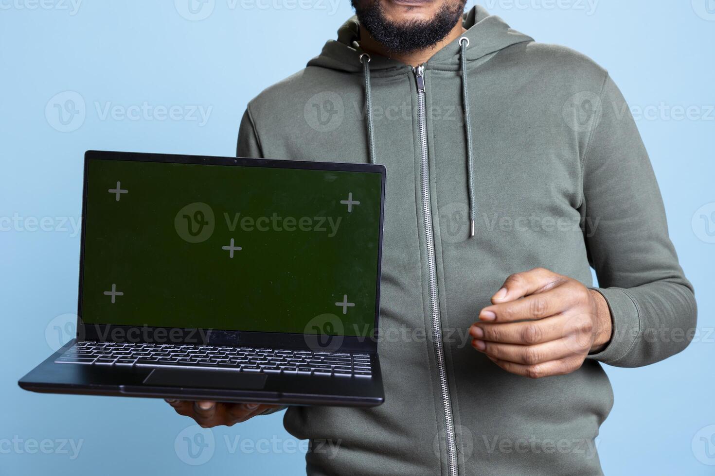 Jolly african american person presenting green screen display on laptop, doing recommendation. Friendly young guy pointing at mockup on notebook, wearing casual clothes in studio. photo