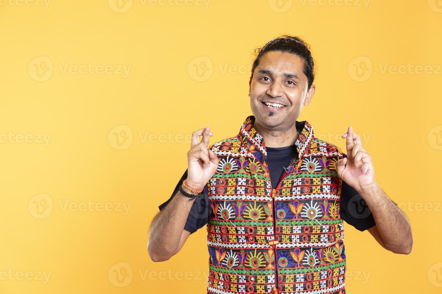 Portrait of joyous man crossing fingers, waiting to receive good news, isolated over studio background. Radiant person with positive mood hoping for good luck, aspiring for miracle photo