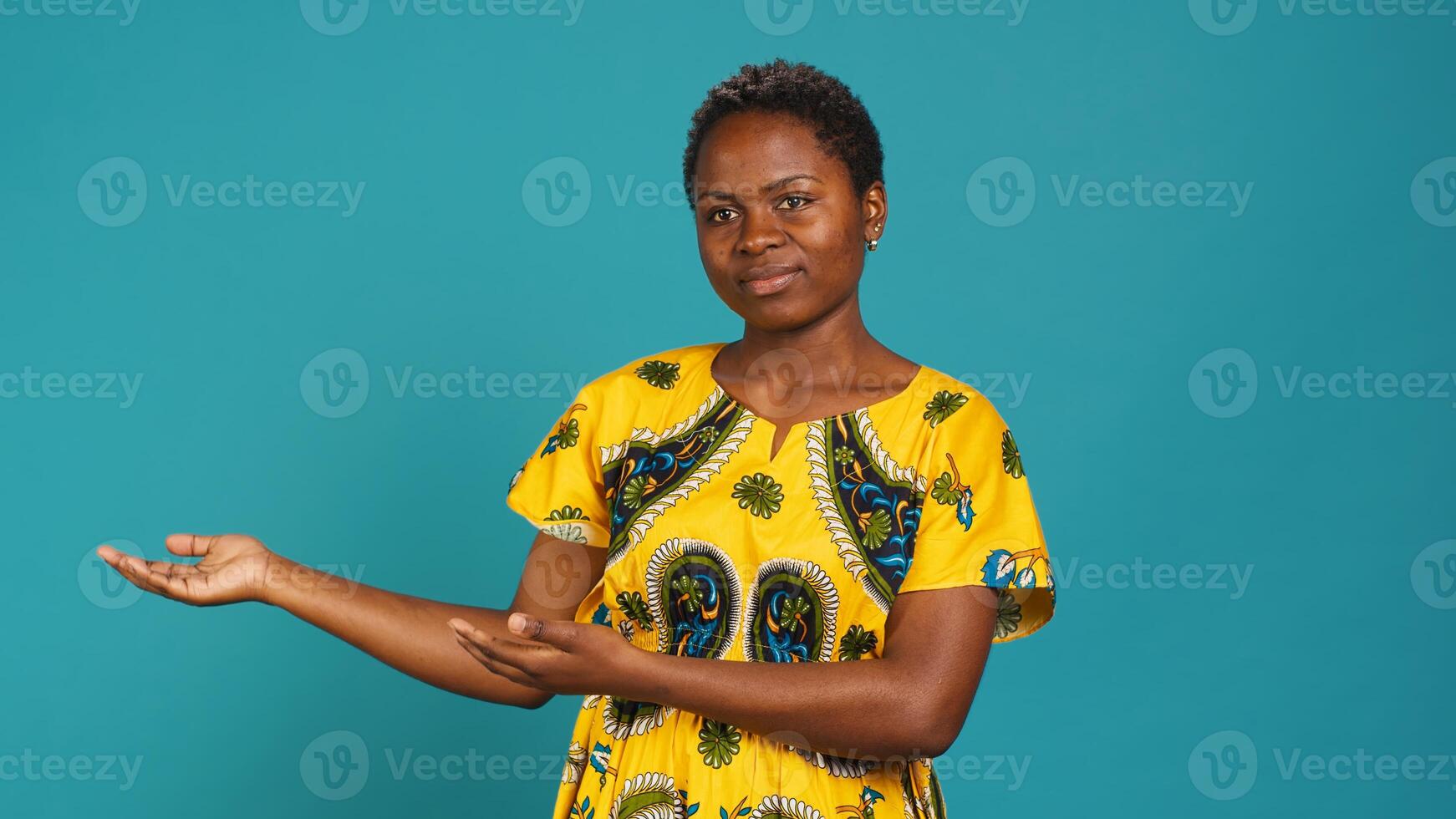 Confident smiling girl indicating direction to left or right sides in studio, pointing her index fingers around. Young natural person wears traditional african attire with tribal native elements. Camera A. photo