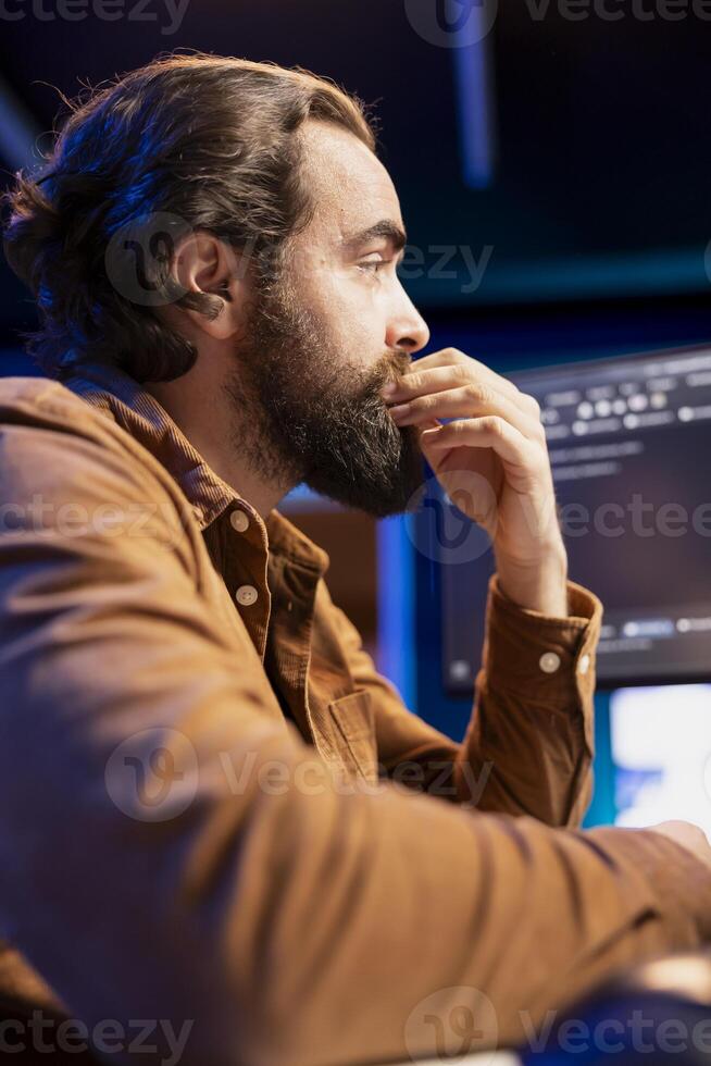 Cybersecurity professional anxiously looking at computer screen, trying to find company security loopholes and injected viruses. Programmer carefully reading lines of code on desktop PC monitor photo