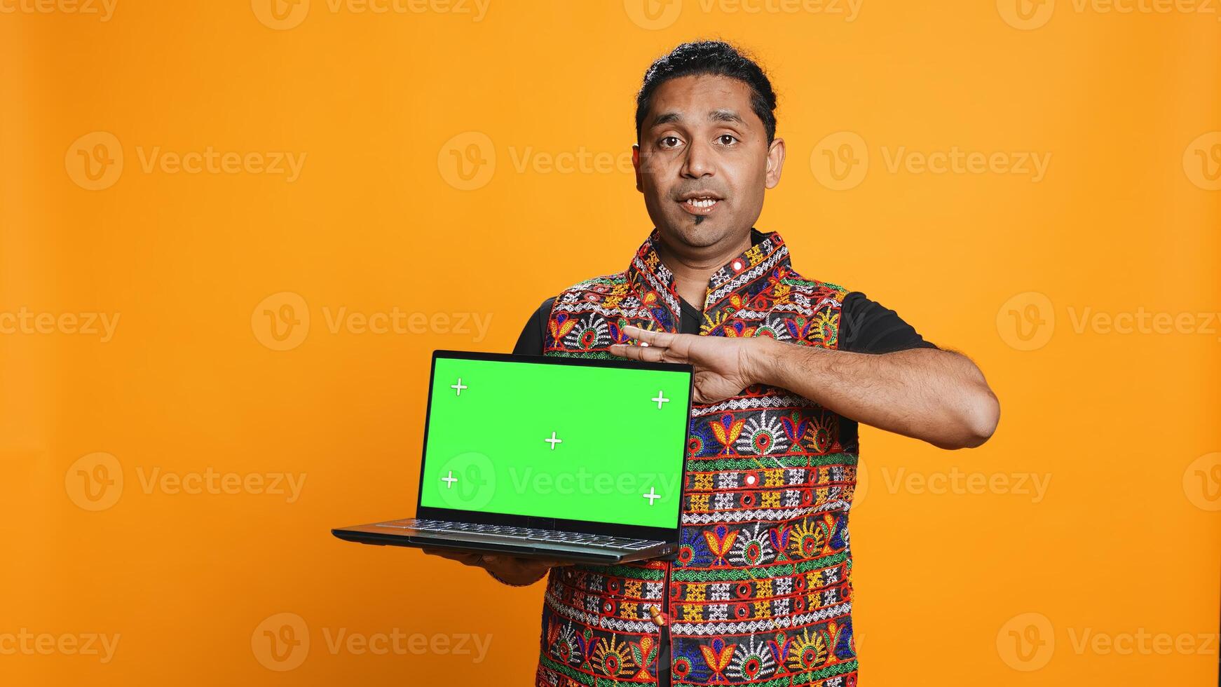 Upbeat tech specialist doing promotion using isolated screen laptop, studio background. Cheerful indian person holding chroma key notebook, doing advertisement for it, camera B photo