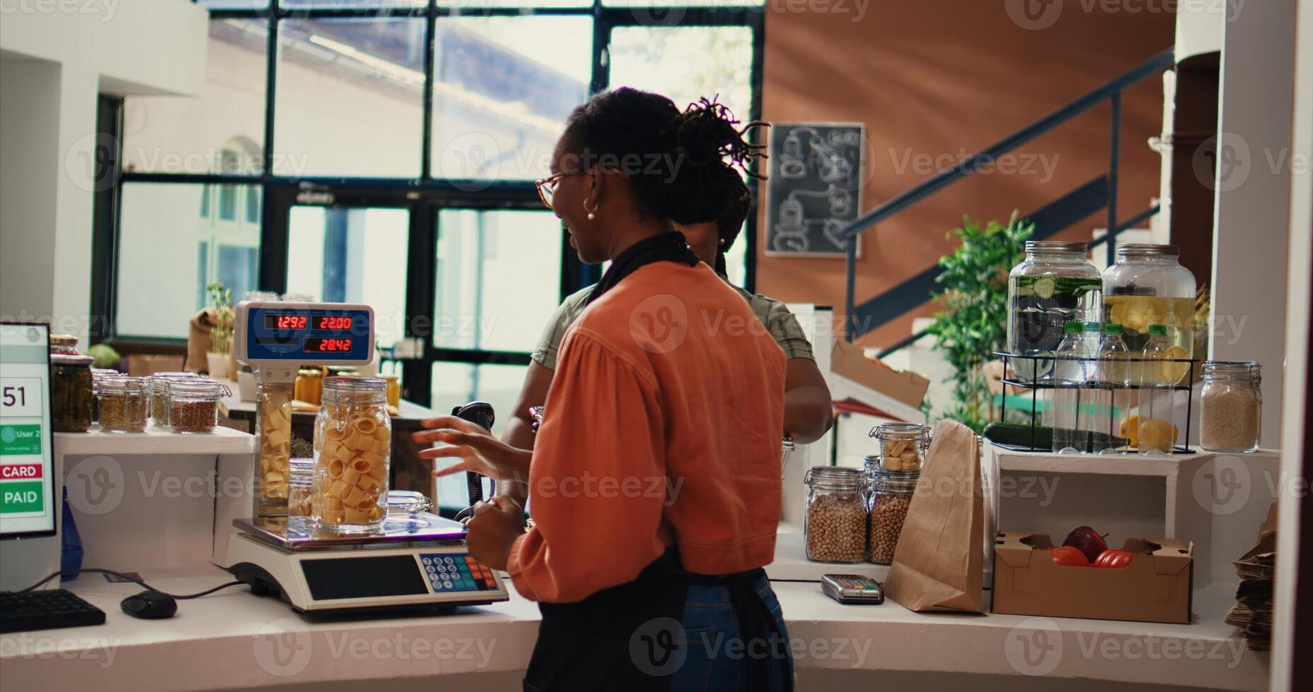 Buyer approaching checkout counter to pay for goods at eco friendly store, choosing various produce and bulk items. Vegan woman going grocery shopping at organic shop. Handheld shot. photo