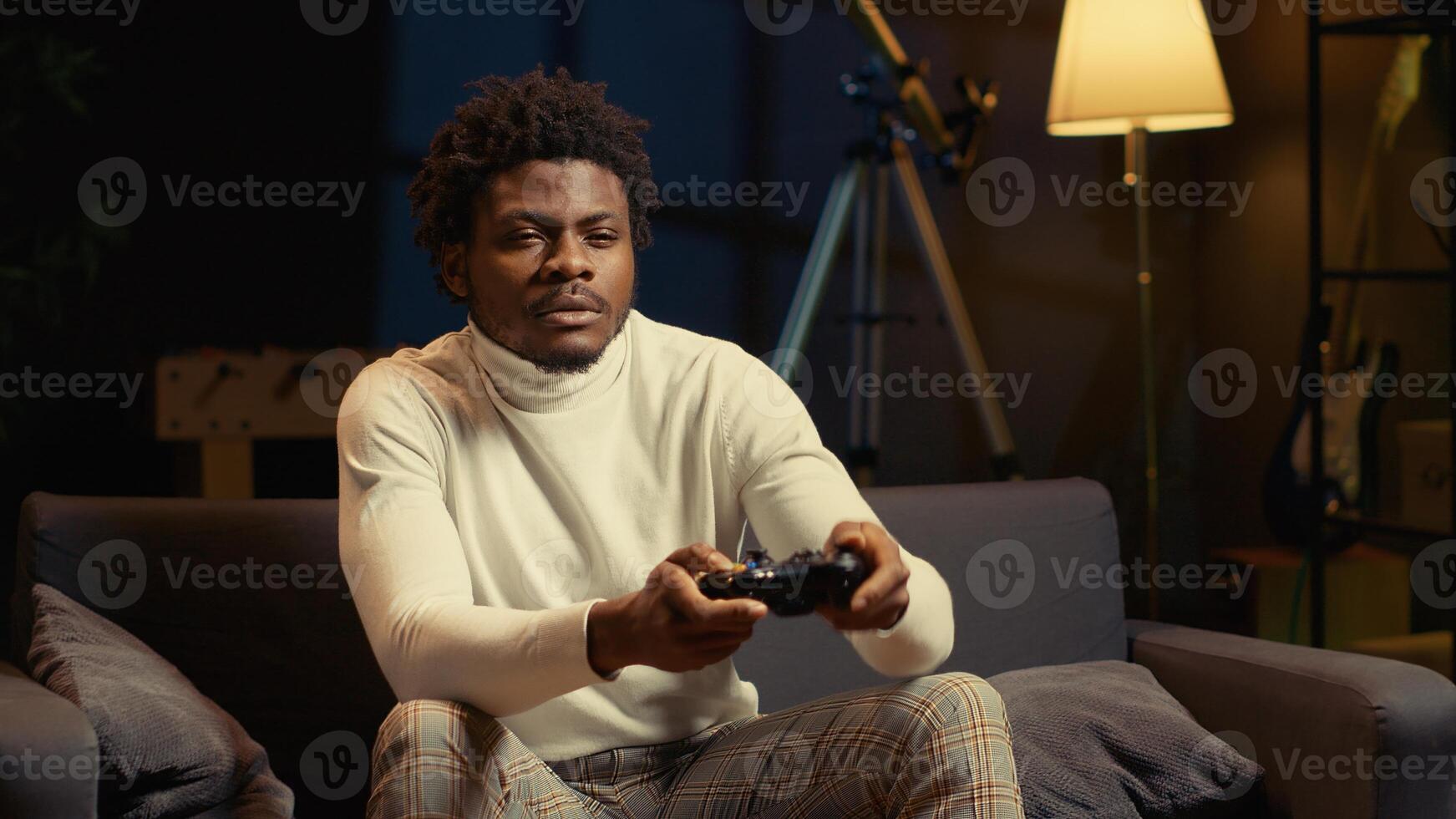 Focused BIPOC man plays intense online videogame, spamming attack buttons on controller. Gamer participating in internet esports competition, sitting on couch and playing on gaming console photo