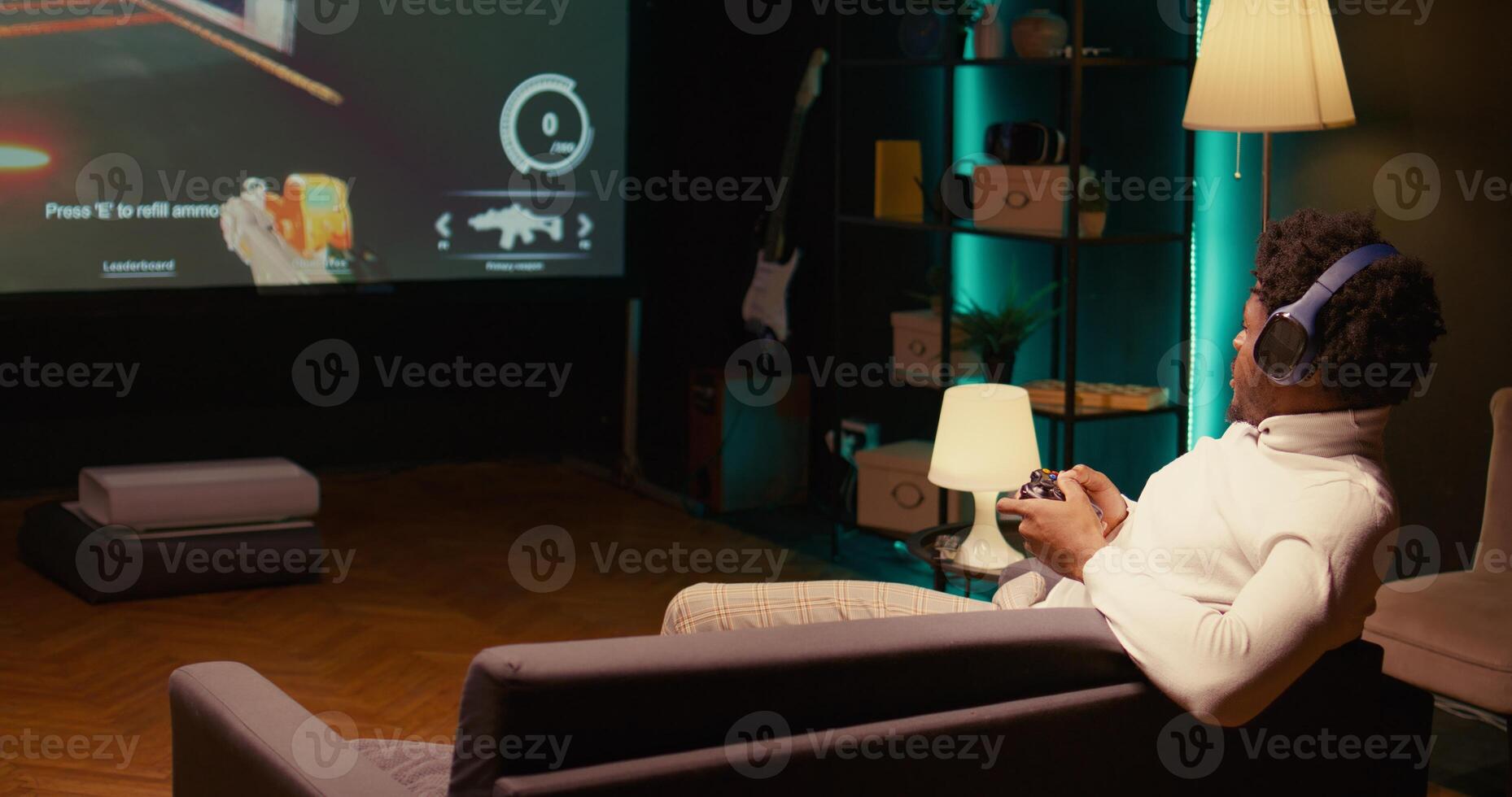 African american player playing SF FPS videogame on big smart TV, having fun in dark apartment room. Gamer putting headphones on to talk with teammates while competing in online multiplayer game photo