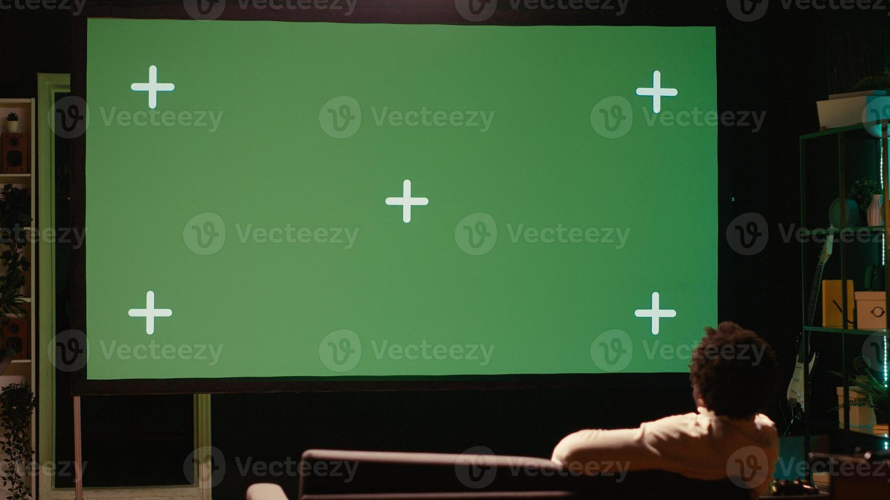 Man zapping through green screen TV channels using remote, relaxing on couch in living room used as home theatre. Person using chroma key television set to entertain himself photo