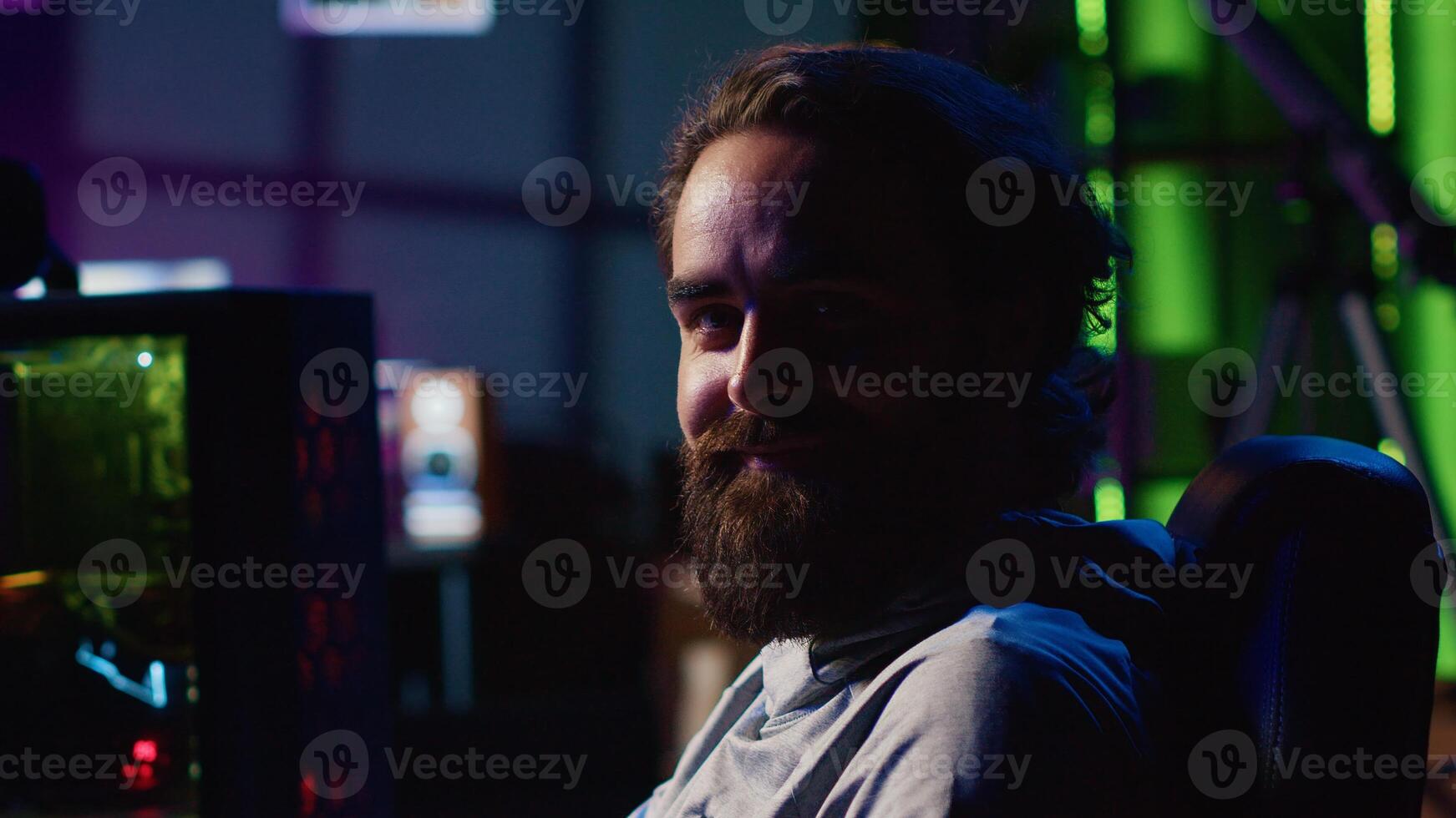 Man in dark living room playing games on gaming PC at computer desk during leisure time. Gamer battling enemies in online multiplayer shooter from neon lights ornate home photo