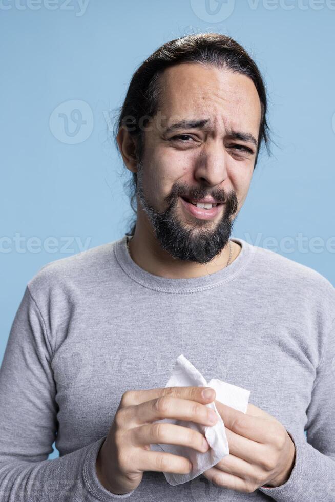 Male model dealing with a heartbreak and crying in studio, wiping his tears with a handkerchief and whining. Young sad man feeling unhappy and distraught, desolation and low self esteem. photo
