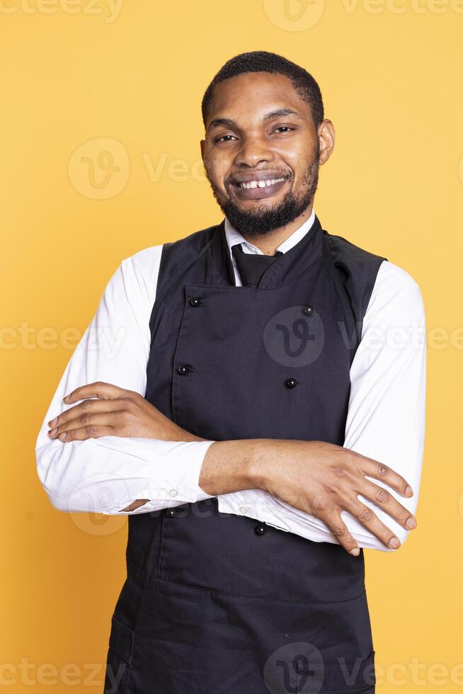 Portrait of restaurant waiter wearing professional uniform and apron, getting ready to assist and serve clients. Employee working in service oriented environment for customer satisfaction. photo