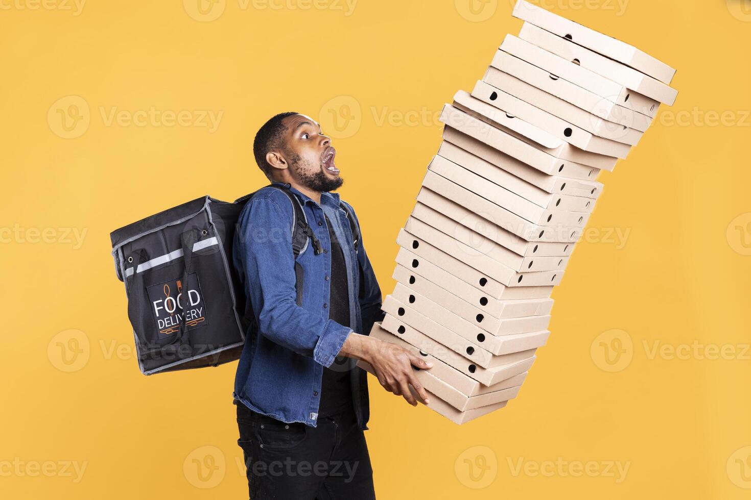 Clumsy african american deliveryman dropping a huge stack of boxes, wasting a lot of pizza and making a mess. Young courier does a mistake and spills a large pile of fast food, reckless accident. photo