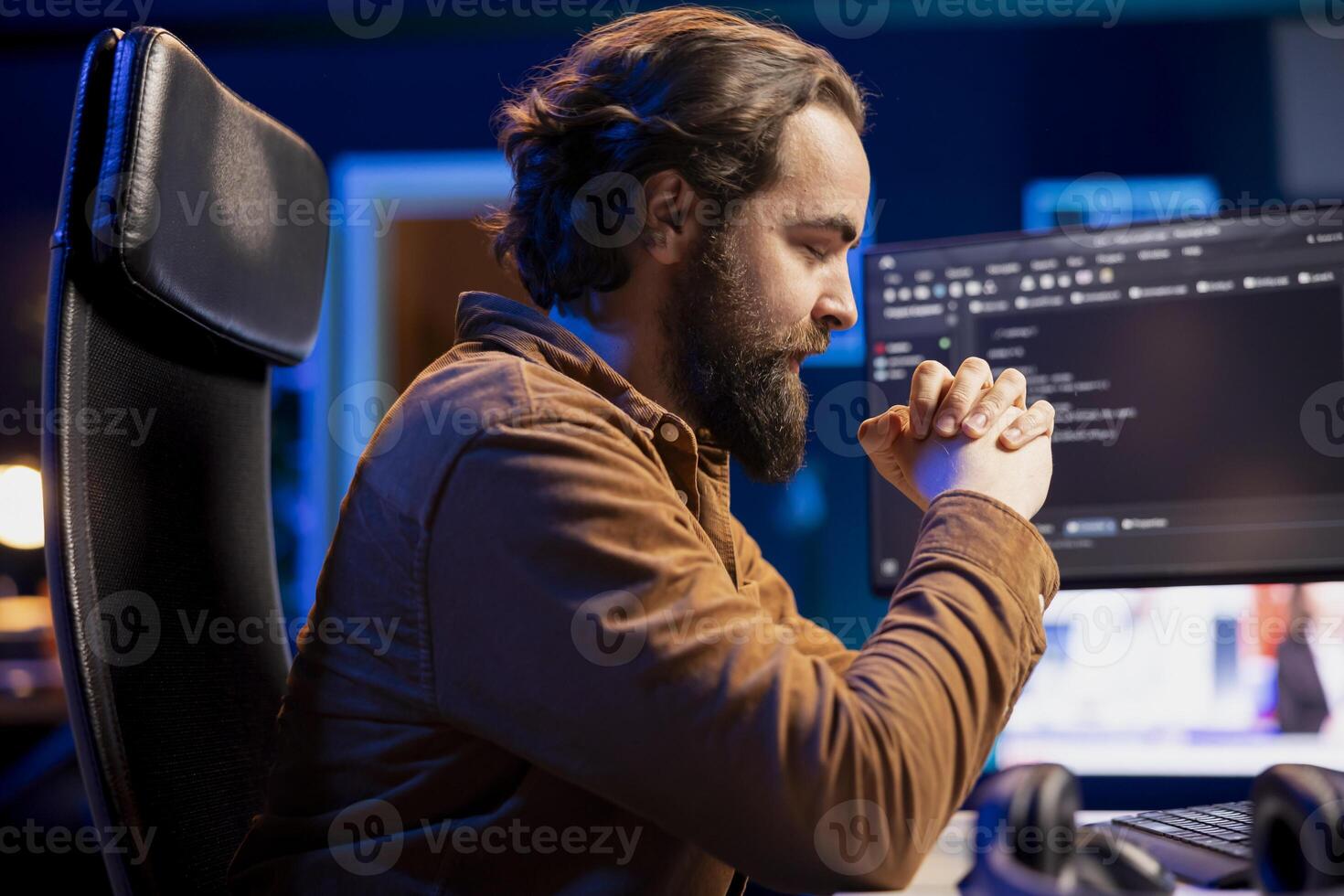 Developer closing eyes while sitting at computer desk, trying to relax eyes after looking at monitors all day. Programmer feeling fatigued after reading too many lines of code on PC screen photo