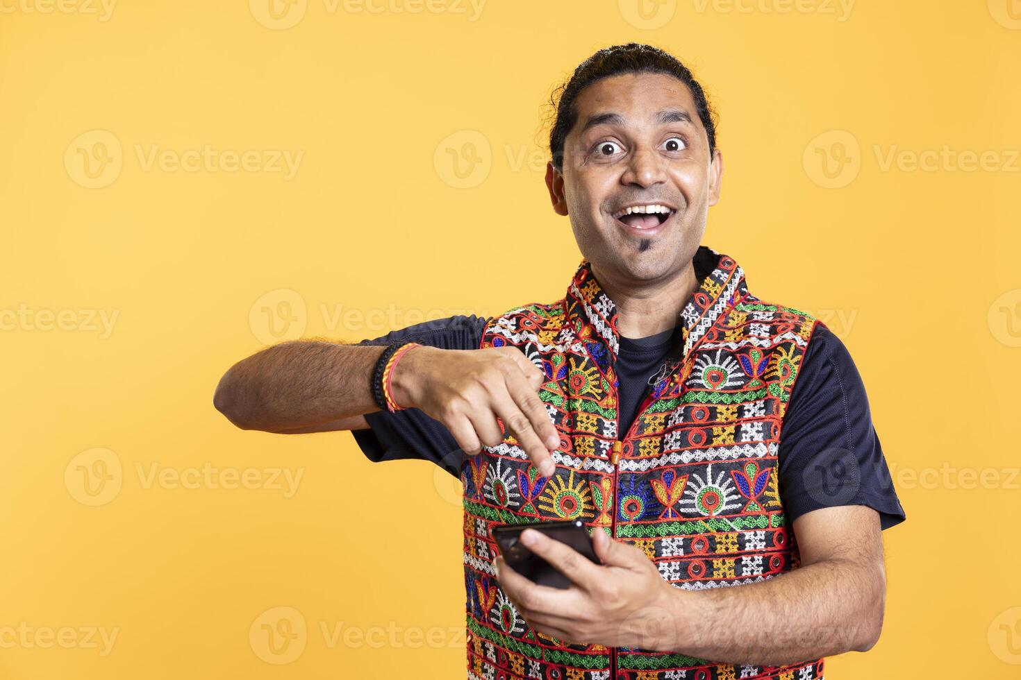 Portrait of awestruck person using cellphone, feeling excited after seeing picture on social media feed. Amazed indian man clicking phone screen with finger, feeling ecstatic, studio background photo