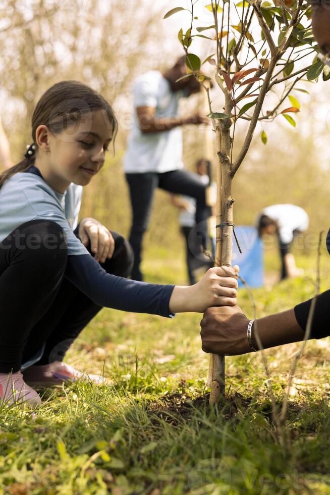Young girls volunteering to protect the natural habitat and plant trees, team up to increase vegetation. Activist child covering holes and installing greenery, protecting the ecosystem. photo